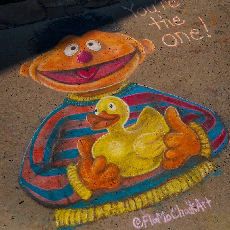 Chalk art on pavement depicting Ernie from Sesame Street holding a yellow rubber duck, with the words Youre the one! written above and @FloMoChalkArt in the corner.